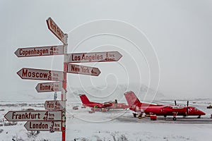 Route direction pole with different cities and North Pole with red planes in the background, Kangerlussuaq airport, Greenland