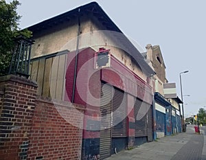 A row of abandoned stores with boarded up shop fronts with crumbling facades and peeling paint in an urban road