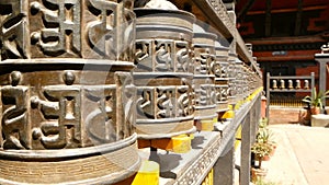 Row of aged religious prayer wheels or drums with mantra Om Mani Padme Hum in yard of temple, Durbar Square, Nepal