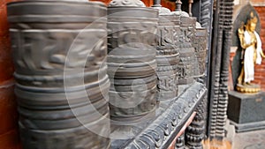 Row of aged religious prayer wheels or drums with mantra Om Mani Padme Hum in yard of temple, Durbar Square, Nepal