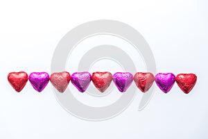 Row of alternating pink and red foil wrapped chocolate hearts on white background