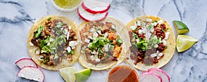 Row of assorted mexican street tacos with garnishes in wide banner composition photo
