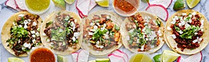 Row of assorted mexican street tacos with garnishes in wide banner composition photo