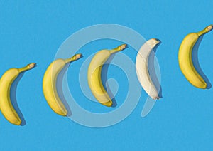 Row of bananas on blue background, one is peeled