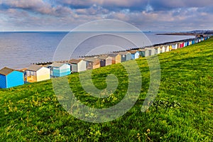 Row of beach huts along the coast in Tankerton, Whitstable, Kent. The green grass slopes are behind the huts and groynes photo