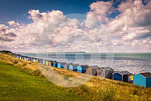 Row of beach huts under a white cloudscape along the coast in Tankerton, Whitstable, Kent.