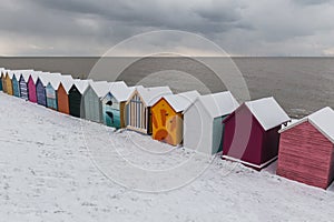 Row of beach huts in winter snow on coast of Herne Bay, Kent, En