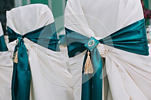 Row of beautiful chairs decorated with fabric and bows of green color in the wedding hall