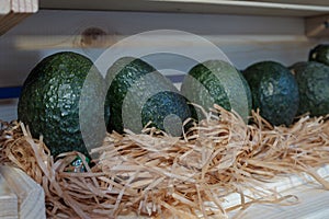 Row of big green organic avocados in a wooden shelf