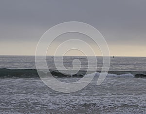 Row boats in the pacific in Santa Monica, cloudy sky after sunset, a sailboat to the right, one little wave in the foreground