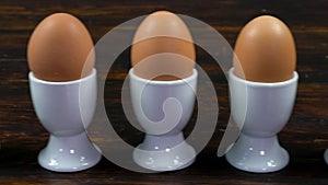 Row of boiled eggs in white egg cups from one egg that has a happy smiling face drawn on it