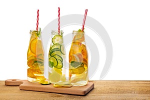 row of bottles lemonade with lemon, orange, lime, twig mint, cucumber, ginger and straws on wooden background isolated, concept o