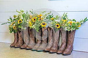 Row of brown cowboy boots with bouquets of flowers for a wedding ceremony
