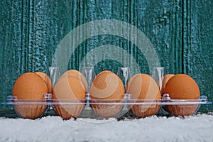 A row of brown fresh eggs in open plastic packaging in white snow against a green wall