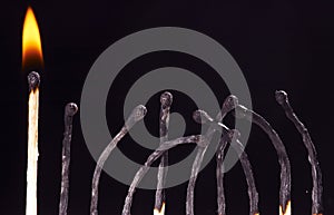 Row of burned-out matches over the black background. one match is burning