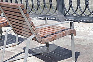 A row of chairs with wooden seats covered with snow near a metal fence on the canal embankment.