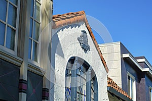 Row of close up house facades with white and brown faces with red adobe tiles on roof and a blue sky background in late