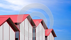 Row of cold storage warehouse buildings with white sandwich panel wall and red metal gable roof against blue sky