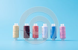 In a row colored spools of sewing thread on a blue background. fighting squad with a needle