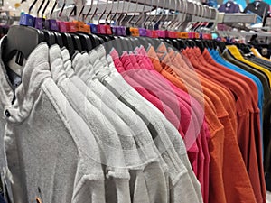 Row of colorful Apparel on Shoulders Hangers of T-Shirts of Retail Shop with other Items on Background, interior of cloth store