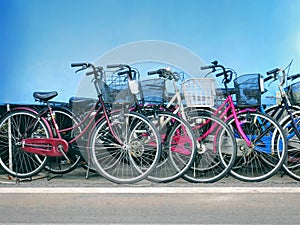 Row of Colorful Bicycles with Front Baskets Parked By the Road Against Blue Wall