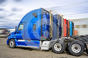 Row of the colorful big rigs semi truck tractors without semi trailers standing on the industrial parking lot waiting for the next