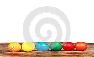 Row of colorful Easter eggs on a wooden table with a white background