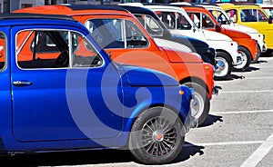 A row of colorful Fiat 500s  in a roadside parking lot, waiting to participate in an auto gathering later.