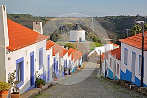 A row of colorful houses along a steep cobbled street inside Odeceixe near Aljezur, leading to a whitewashed traditional windmil