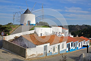 A row of colorful houses along a steep cobbled street inside Odeceixe near Aljezur, with a whitewashed traditional windmill, Cos