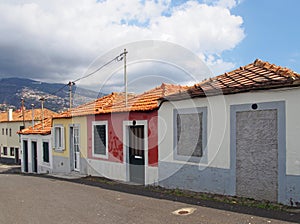 A row of colorful old painted single story houses on a sloping street in funchal madeira in bright sunlight with blue sky