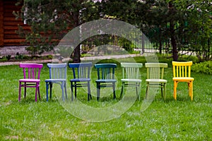 a row of colorful rainbow wooden chairs on a green lawn, an LGBT community party in the park in the month of LGBT pride