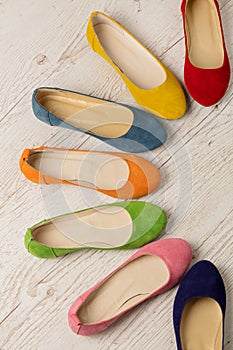 Row of colorful shoes ballerinas on a white wooden background.