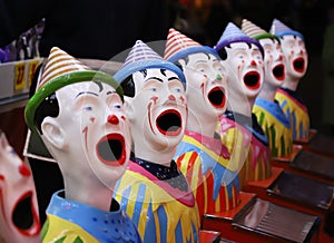 A row of colourful toy clowns with open mouths, an attraction at a fair