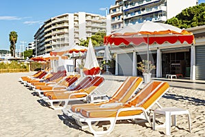 A row of deck chairs with orange mattresses on a sandy beach in a resort town. Bright sunny day