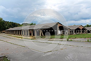 Row of densely built wide hangar buildings with destroyed support walls and unusual bent roofs at abandoned military complex