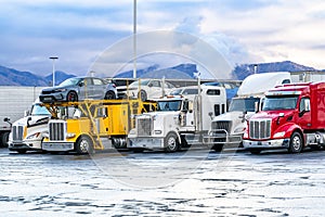 Row of a different big rigs semi trucks with semi trailers standing on the truck stop parking lot according to the traffic