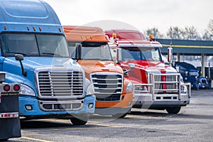 Row of different big rigs semi trucks on truck stop parking lot waiting for continuation of the road routes