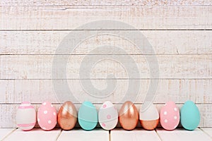 Row of Easter eggs on white wood. Rose gold, pink, turquoise and white.