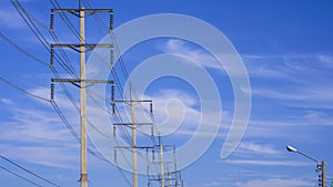 Row of electric power poles with cable lines against white cloud in blue sky background