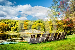 A row of empty chairs under dramatic crisp autumn sky over Tyrrel Lake at Innisfree Garden, Millbrook, New York