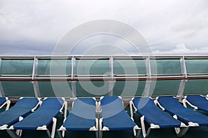 Row of empty deck chairs on the upper deck of a modern cruise ship on a grey and stormy day in the Tropics