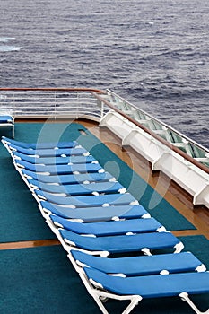 Row of empty deck chairs on the upper deck of a modern cruise ship on a grey and stormy day in the Tropics