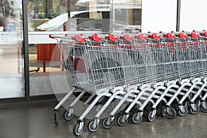 Row of empty metal shopping carts near supermarket outdoors