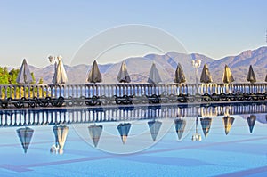 Row of empty sunbeds by the pool and the sea in the morning at dawn. Comfortable high-rise hotel