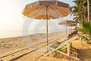 Row of empty wooden beach chairs with parasols on tropical sandy beach in the morning