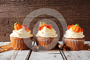 Row of fall pumpkin spice cupcakes with creamy frosting against rustic wood