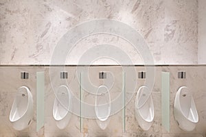 Row of five urinals with infrared sensor, on marble wall, in men's public toilet