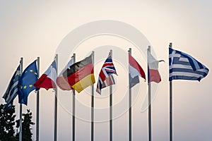 Row of the flags of some European Union countries waving on metal poles against cloudy dusk sky