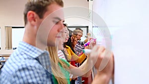 Row of focused students writing on whiteboard in classroom